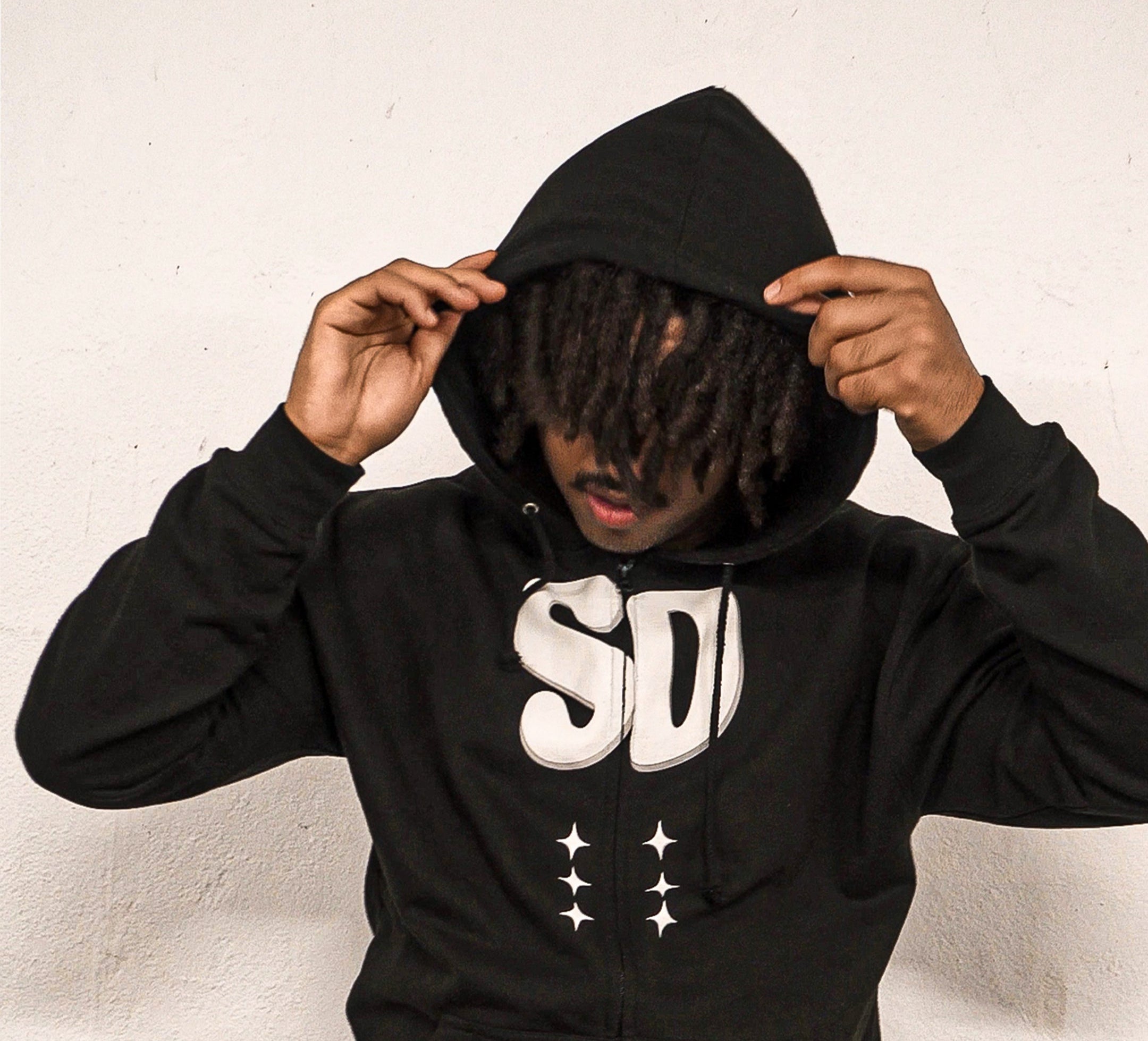 Person wearing a black hoodie with a logo on a light background